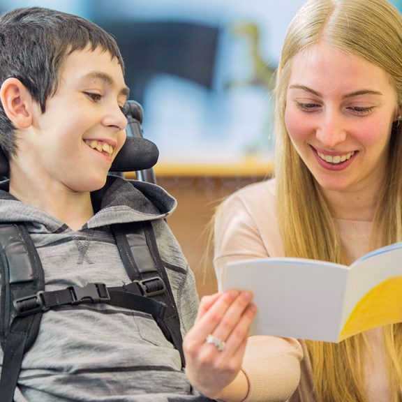 enfant polyhandicapé en train de lire avec une éducatrice